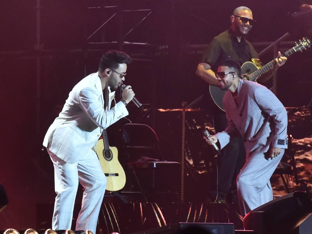 Romeo Santos y Prince Royce abrazados en el escenario saludando al público durante su gira de conciertos.