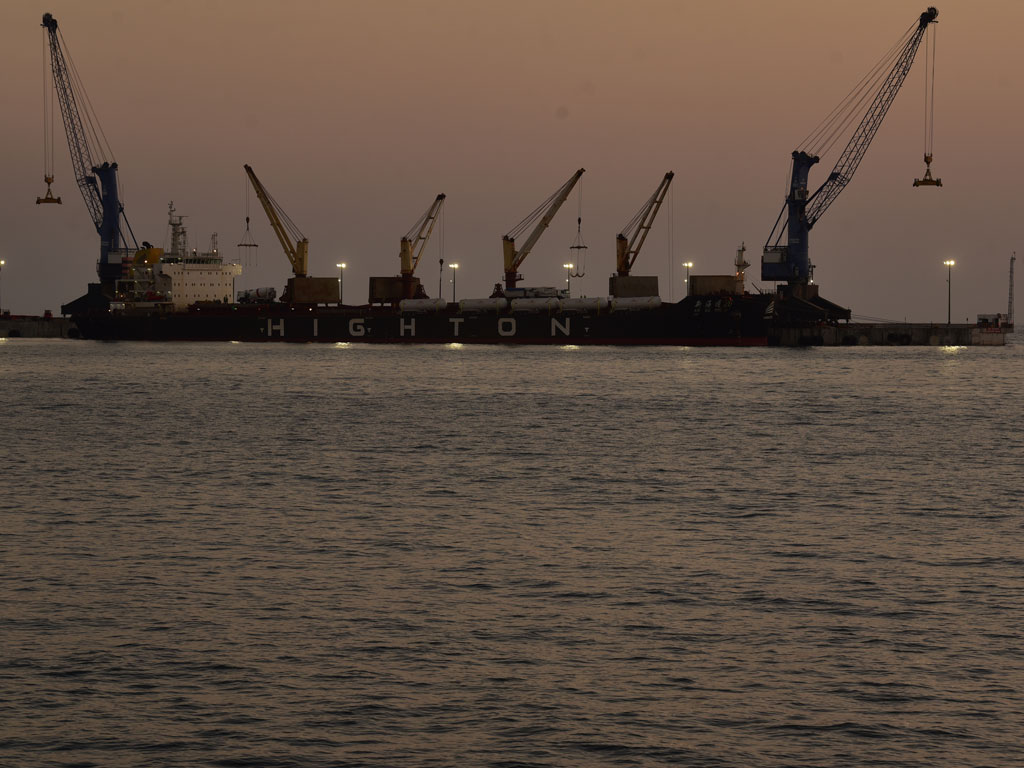 El buque de carga "HIGHTON" atracado en el puerto al atardecer, con sus seis grandes grúas industriales elevándose contra el cielo brumoso.