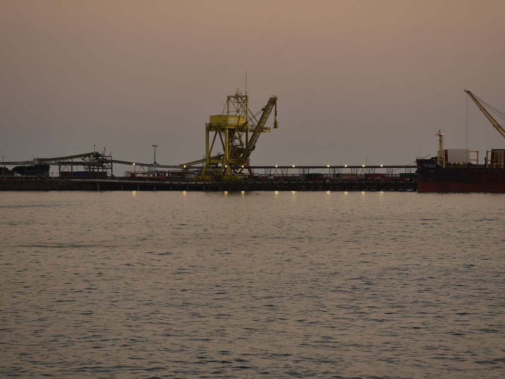 Silueta de un buque de carga con grúas operando en el puerto de Acajutla al anochecer.
