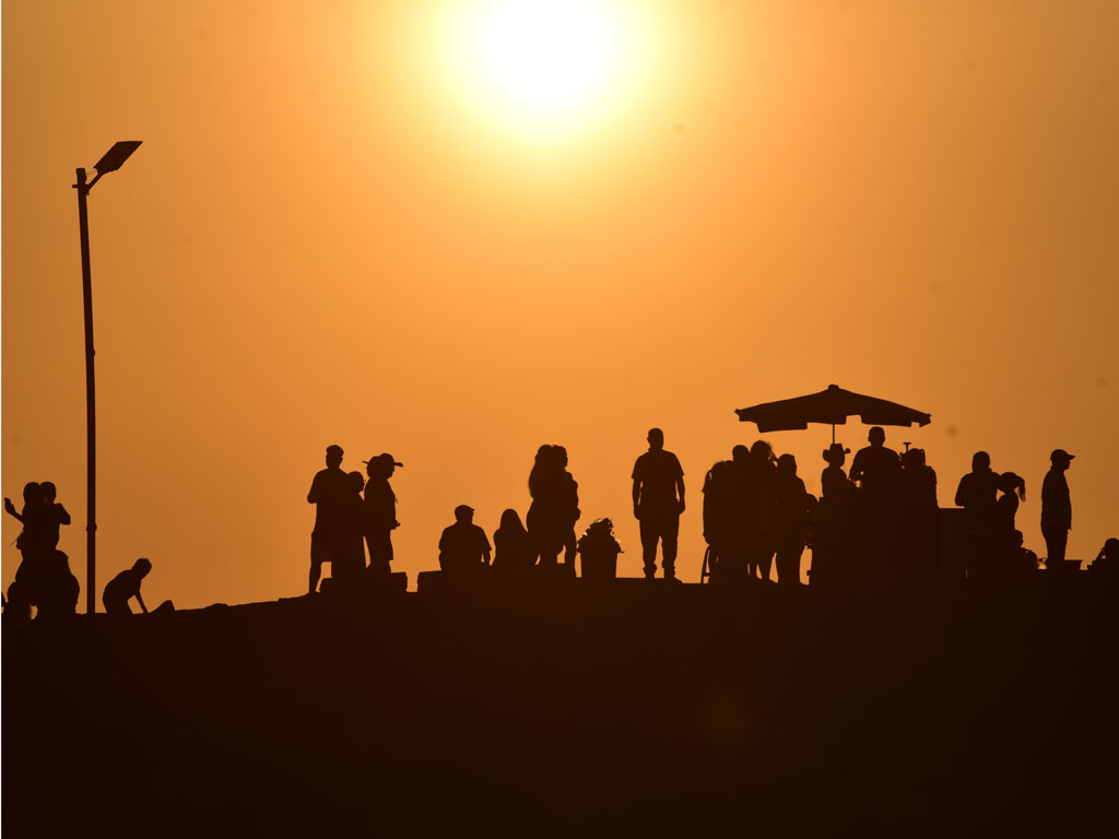 Encuadre cercano en silueta de personas conversando y disfrutando en el muelle bajo la intensa luz del sol. 