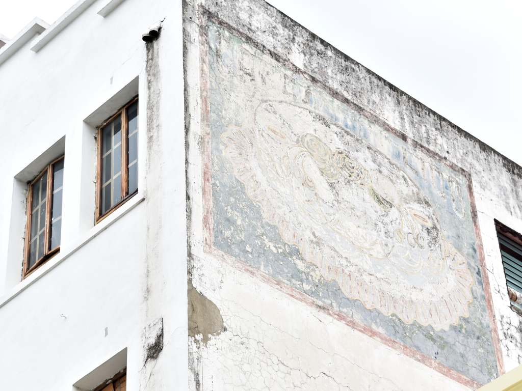 El mural desgastado aporta una capa de textura y color, suavizando la rigidez geométrica de la fachada.