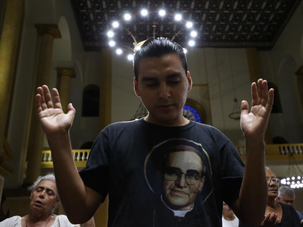 Un fiel reza portando una camiseta con la imagen de San Romero bajo las luces de Catedral Metropolitana.