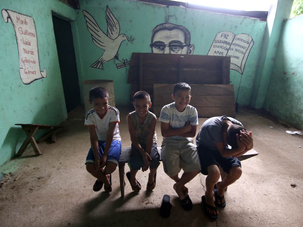 Niños posan frente a un mural con el rostro de San Romero y mensajes de paz.