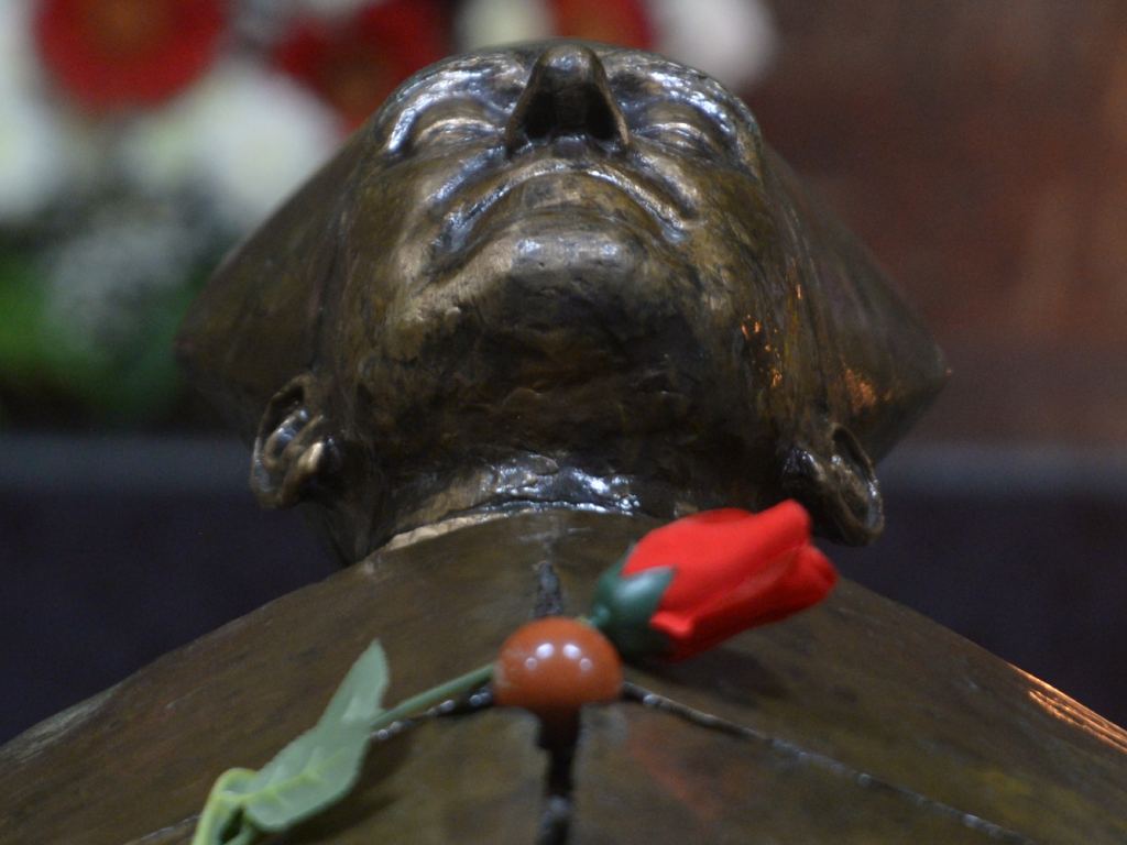 Escultura funeraria de San Romero acompañada por una rosa.