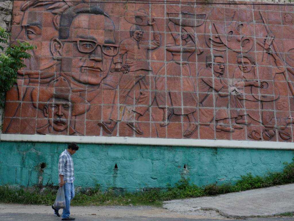 Un hombre camina junto a un gran bajorrelieve de terracota que narra parte de la historia de San Romero y El Salvador.
