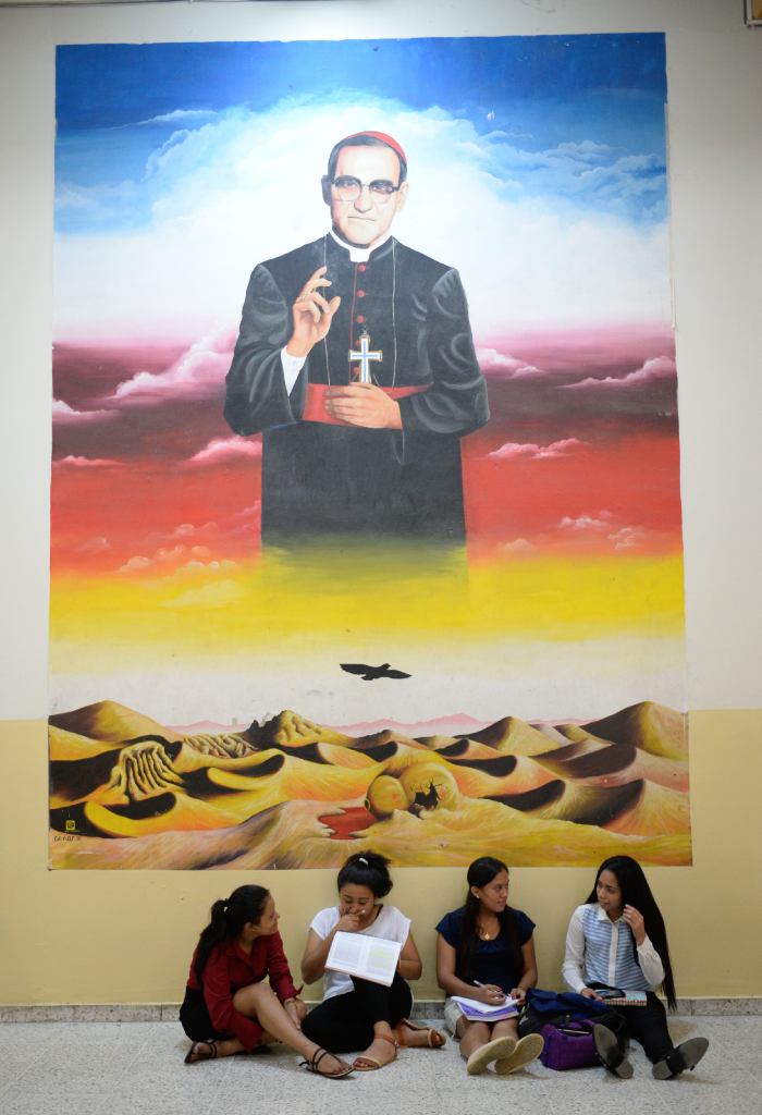 Estudiantes se reúnen bajo un imponente mural de Romero que domina el pasillo.