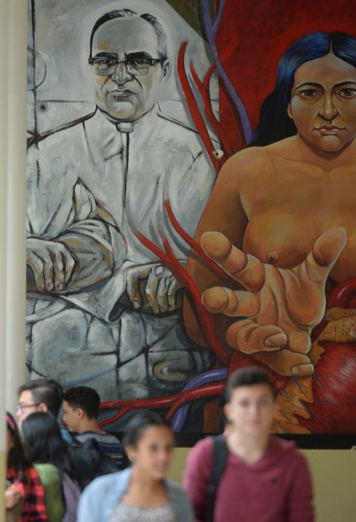 Un mural académico contrasta el retrato del santo con una figura indígena y simbólica, en la Universidad de El Salvador.