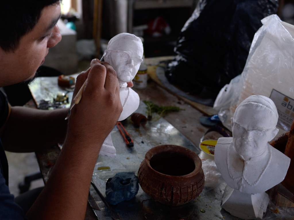 Detalle del proceso de creación, donde un artista esculpe un pequeño busto de yeso.
