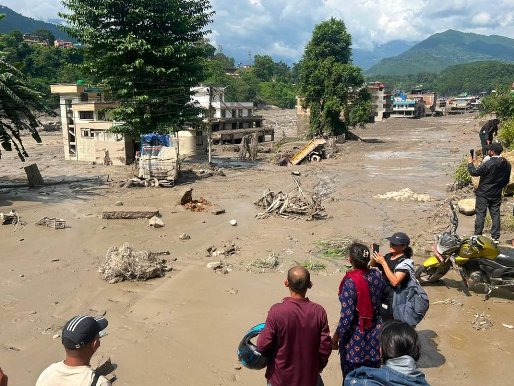 Varios habitantes observan desde un punto elevado viviendas anegadas por un río de lodo gris desbordado en Trishuli Bazar.