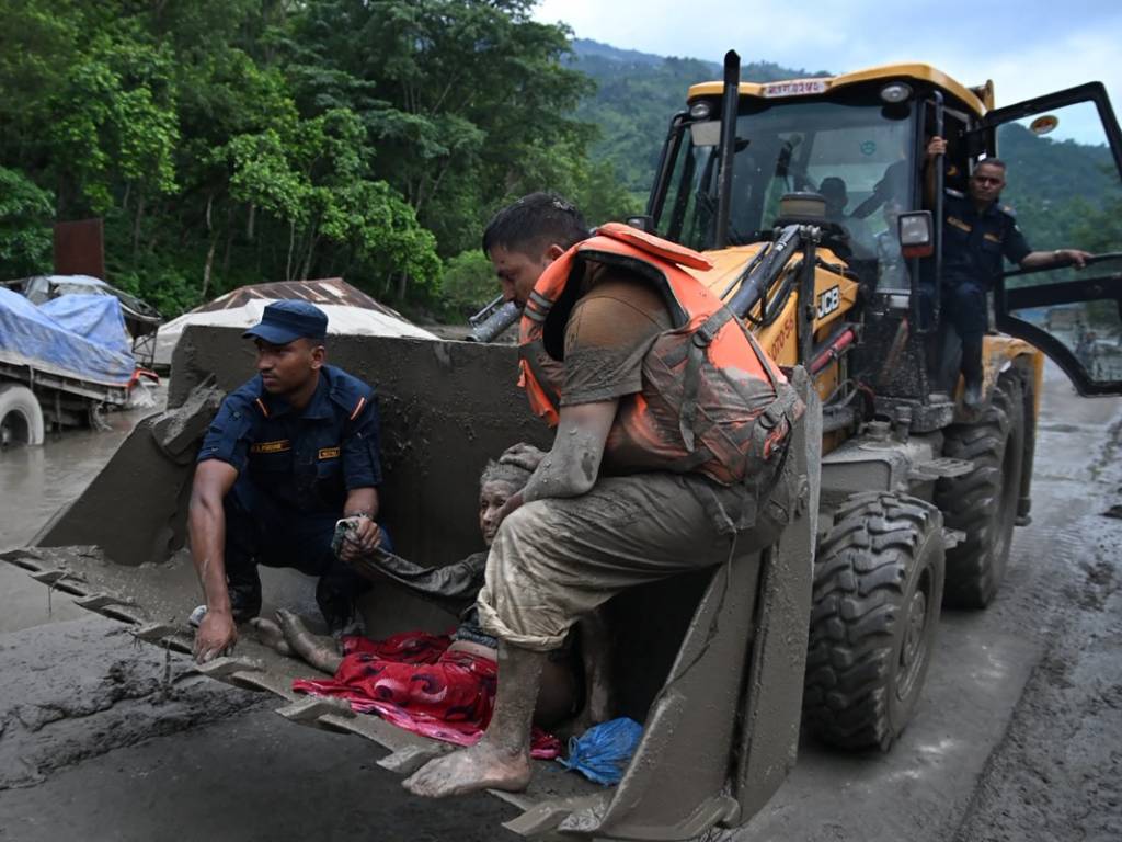 Maquinaria pesada transportando a una persona afectada por las inundaciones en la pala de una excavadora.