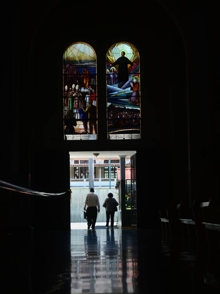 Fieles saliendo de la iglesia bajo la luz de un par de vitrales recién restaurados a ambos lados de la puerta.