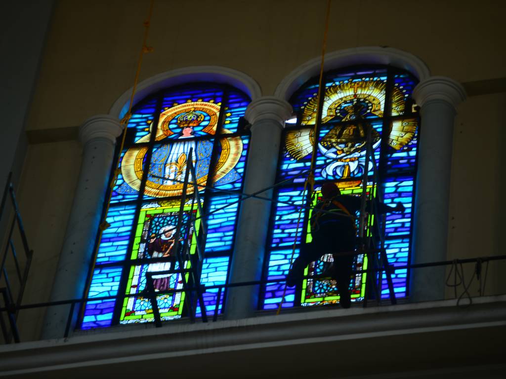 Trabajadores desmontando andamios de metal tras completar la instalación de un gran vitral colorido en una iglesia.