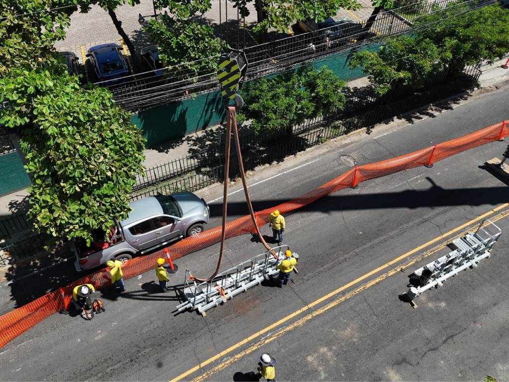 Vista superior de potentes cinchas de izaje sosteniendo una pieza metálica suspendida sobre la zona de la obra.