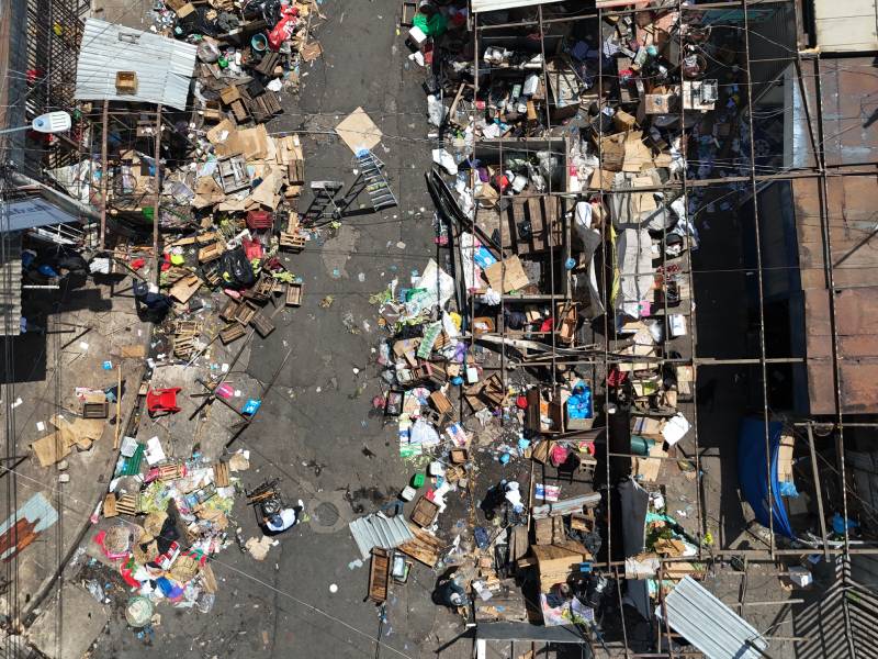 Toma aérea de una calle cubierta de armazones metálicos, cajas de madera, láminas y basura acumulada tras el retiro de puestos.