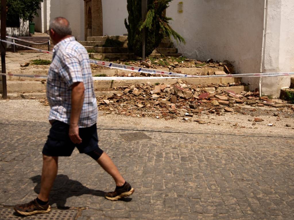Hombre pasando al lado de restos de tejas caídas en la entrada de una iglesia histórica en Granada.