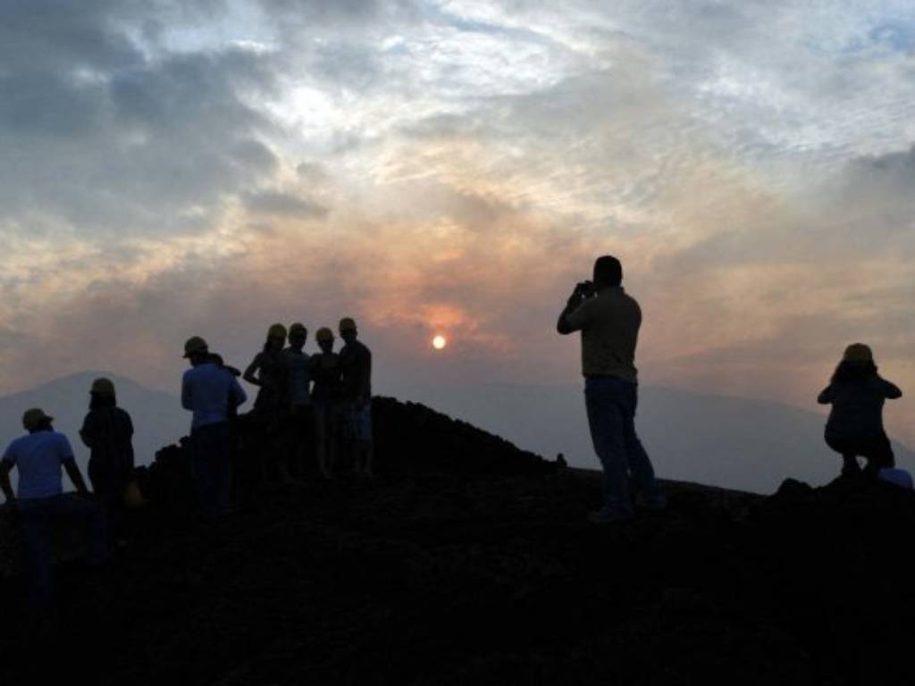 Silueta del complejo volcánico recortada contra un cielo teñido de tonos anaranjados y violetas al atardecer.