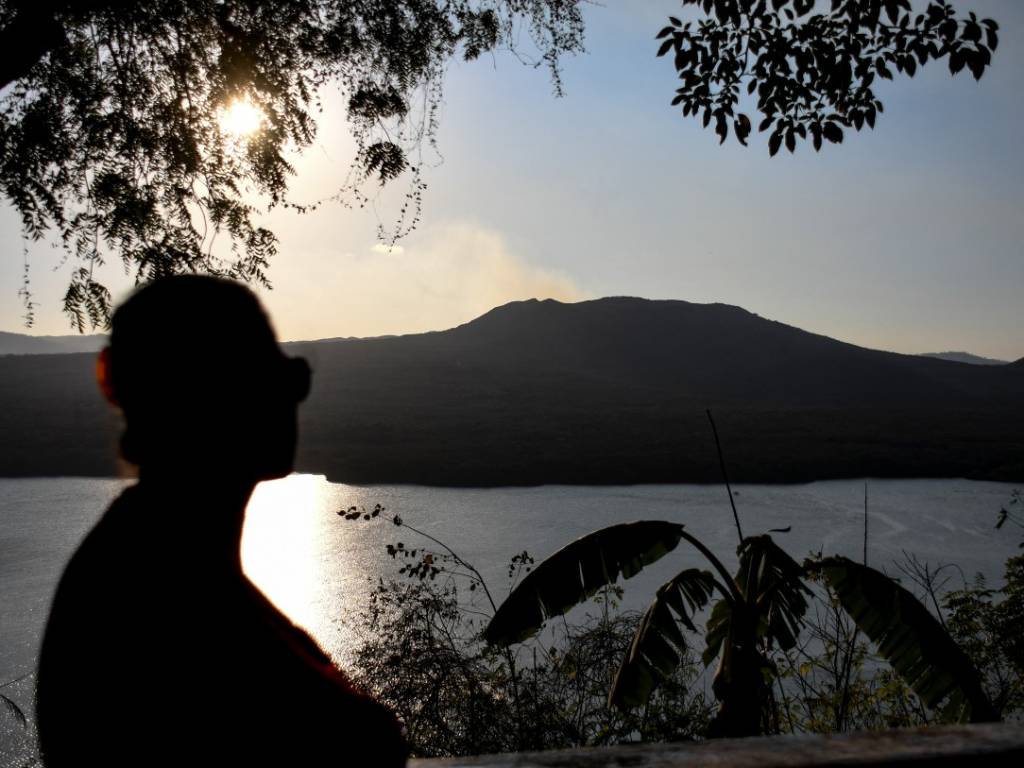 Mujer de espaldas observando el cráter del volcán Masaya y el humo que emerge del fondo.
