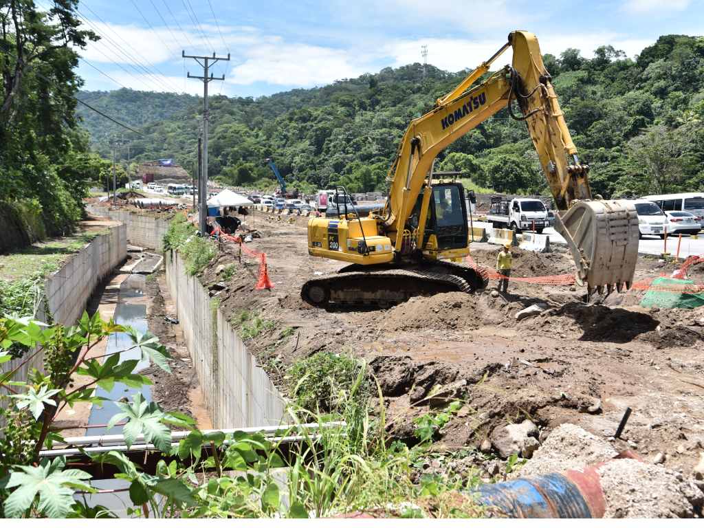Una excavadora trabaja en la adecuación del terreno junto a un canal de drenaje de concreto.