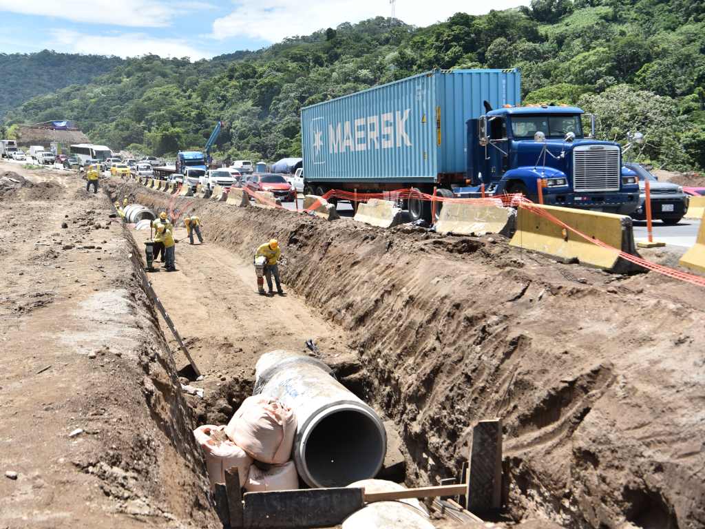 Obreros instalan tuberías de gran diámetro para el drenaje pluvial cerca de la vía principal.
