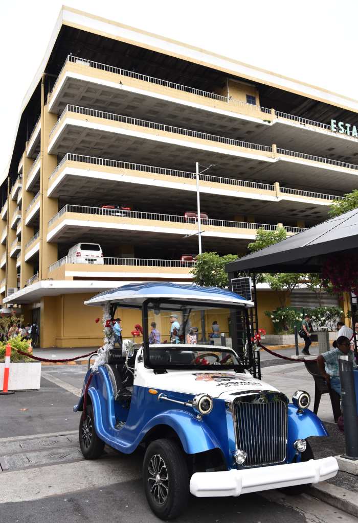 Un vehículo eléctrico azul estacionado frente a un edificio de estacionamientos en el centro de San Salvador.