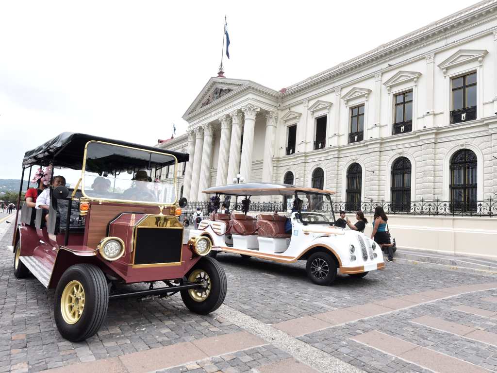 Dos vehículos eléctricos turísticos circulan frente a la majestuosa fachada del Palacio Nacional.