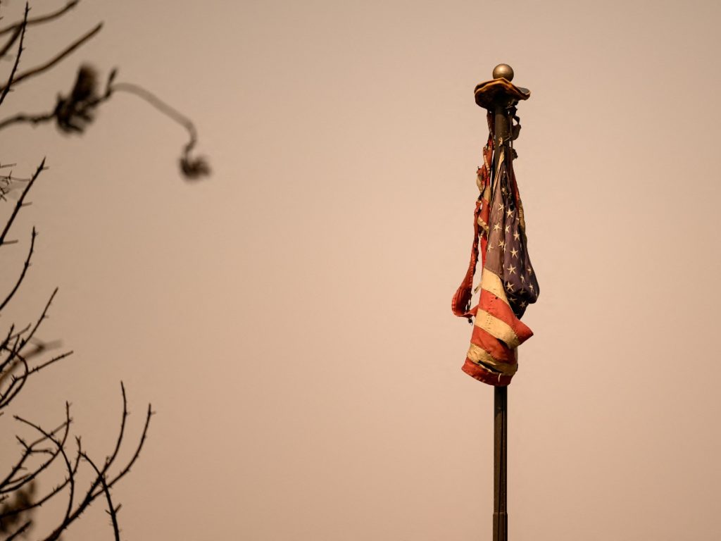 Una bandera estadounidense quemada yace sobre un mástil en una casa destruida por el incendio de Old Trails en Spokane, Washington, el 4 de agosto de 2026.
