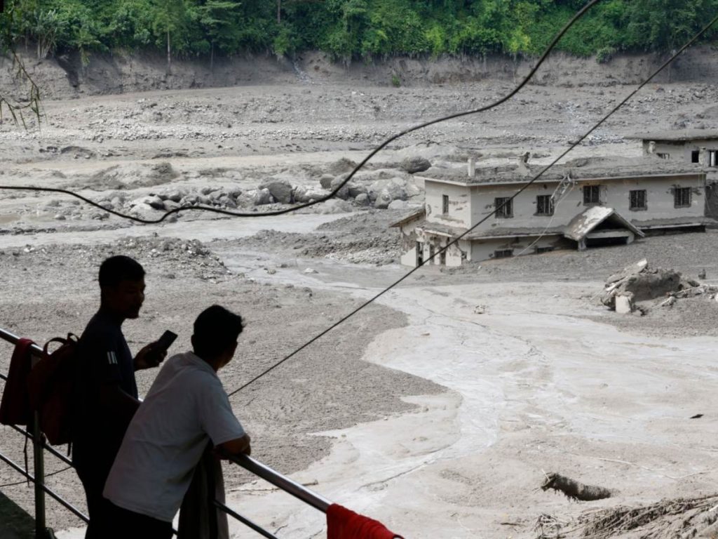 Varias personas observan cómo las aguas de la inundación arrasan Trishuli Bazar tras una crecida repentina, en el distrito de Nuwakot, Nepal, el 26 de agosto de 2026.