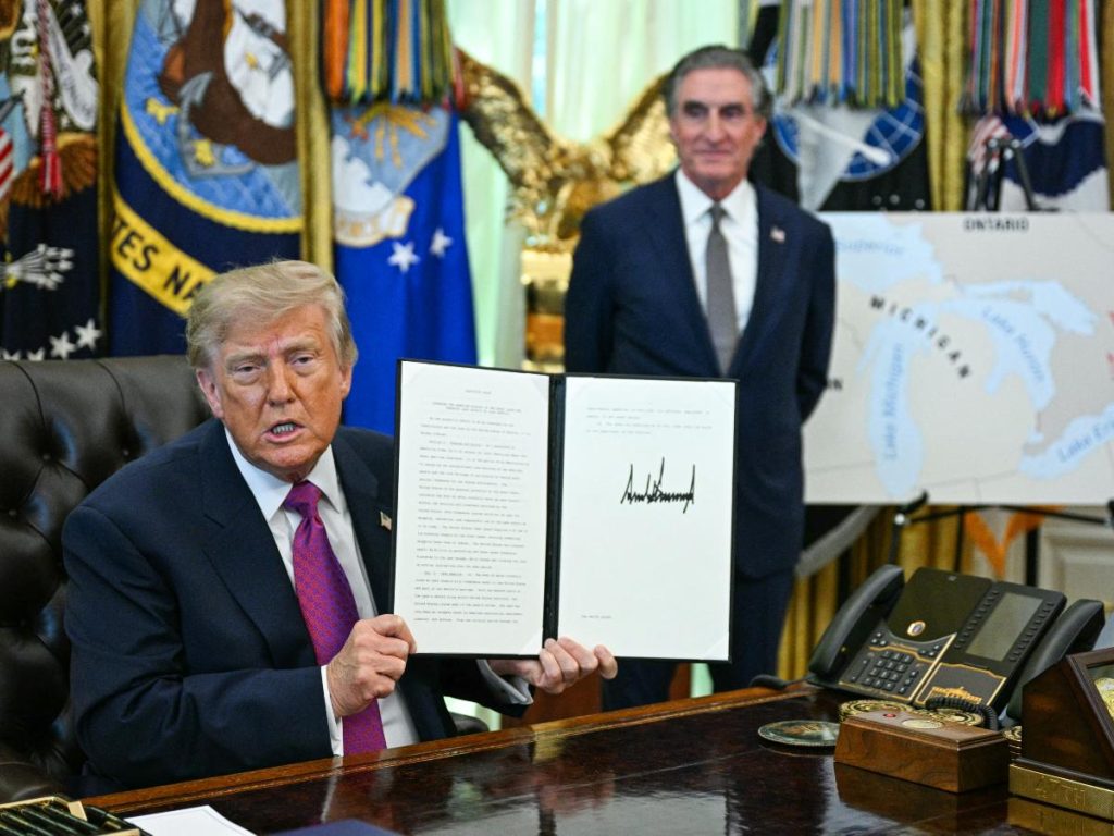 El presidente estadounidense Donald Trump, junto al secretario del Interior Doug Burgum, muestra una orden ejecutiva que firmó para cambiar el nombre del lago Ontario a lago América en el Despacho Oval de la Casa Blanca en Washington, D.C., el 27 de agosto de 2026.