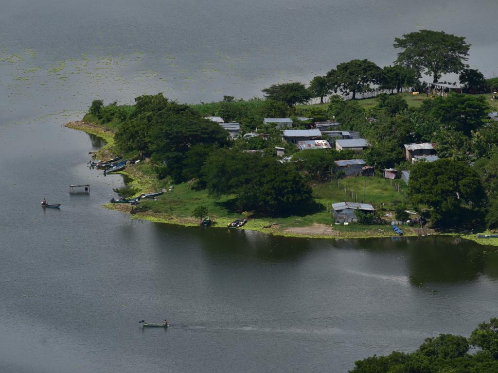 Pequeñas estructuras rústicas se asoman entre la densa vegetación a orillas del sereno lago Suchitlán.