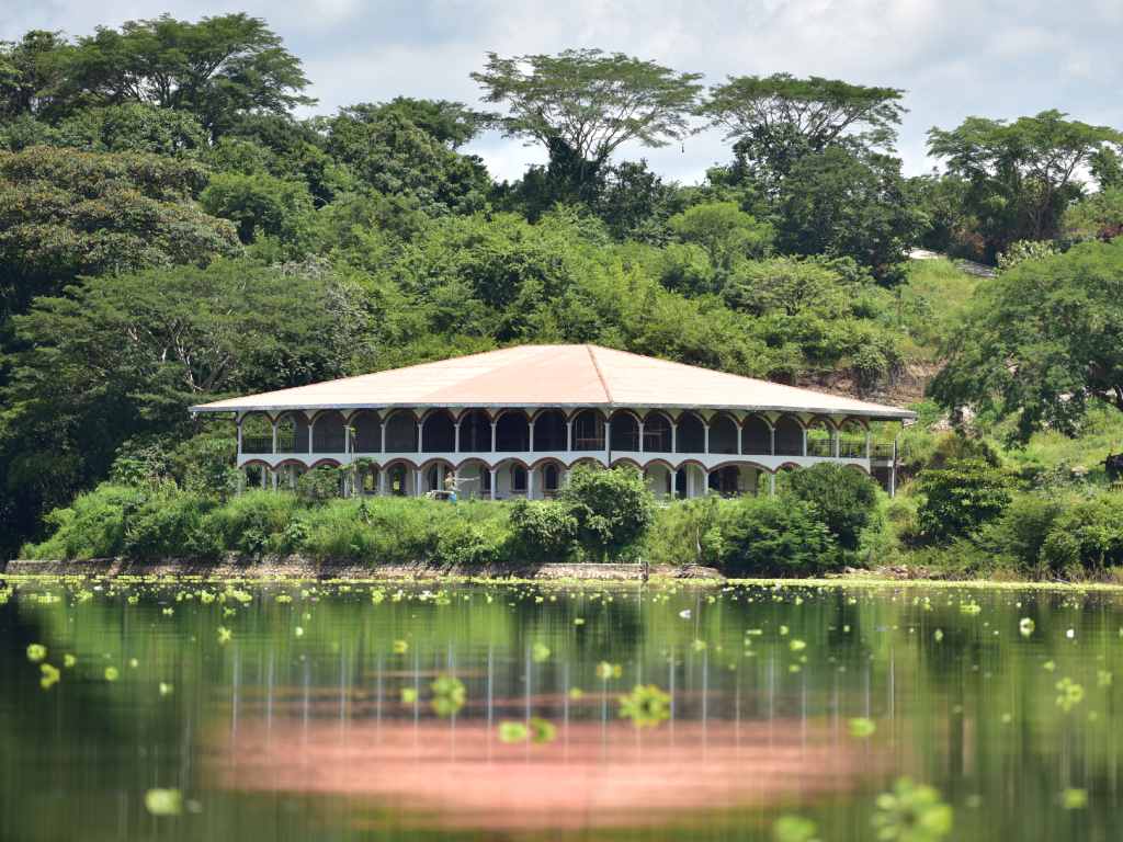 Un edificio distintivo con arcos y techo de tejas se refleja en el agua sembrada de jacintos.
