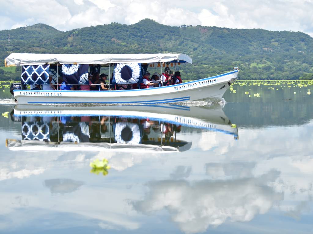 Una lancha techada navega por las aguas tranquilas del lago, reflejando el cielo nublado.