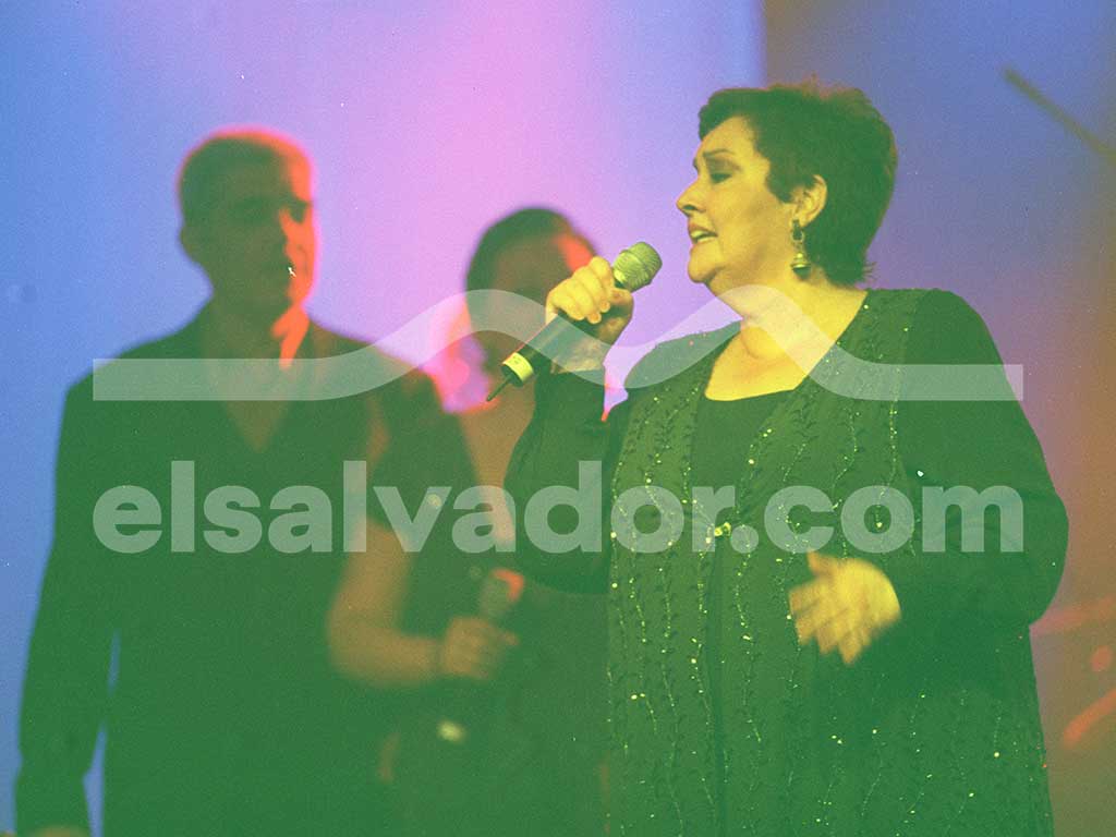Primer plano de Amaya Uranga cantando con los ojos cerrados mientras sus compañeros aparecen desenfocados al fondo.