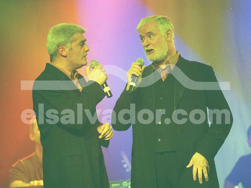 Dos cantantes interactuando y mirándose mientras cantan con micrófonos en mano durante el show.