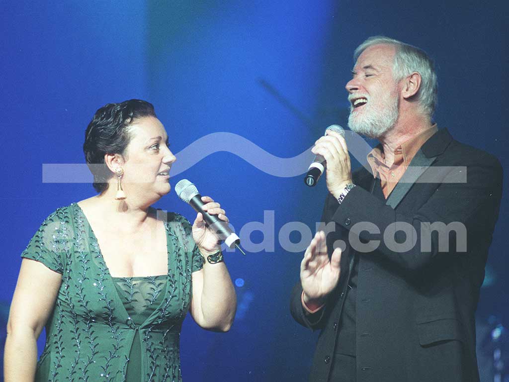 Estíbaliz Uranga cantando un dueto junto a su compañero bajo una intensa luz de fondo azul.