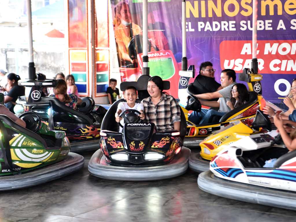 Madres y niños disfrutan juntos entre risas la clásica atracción de los carros chocones.