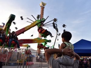 Un niño contempla fascinado las luces y los juegos mecánicos desde los hombros de su papá.