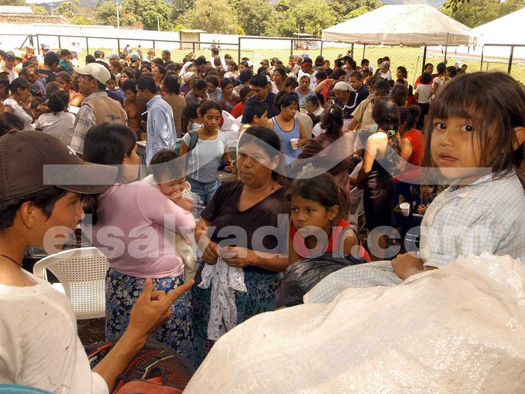 Multitud de personas evacuadas, entre ellas mujeres y niños, aglomeradas en un área abierta con carpas al fondo para recibir ayuda. En primer plano, una niña pequeña mira fijamente a la cámara.