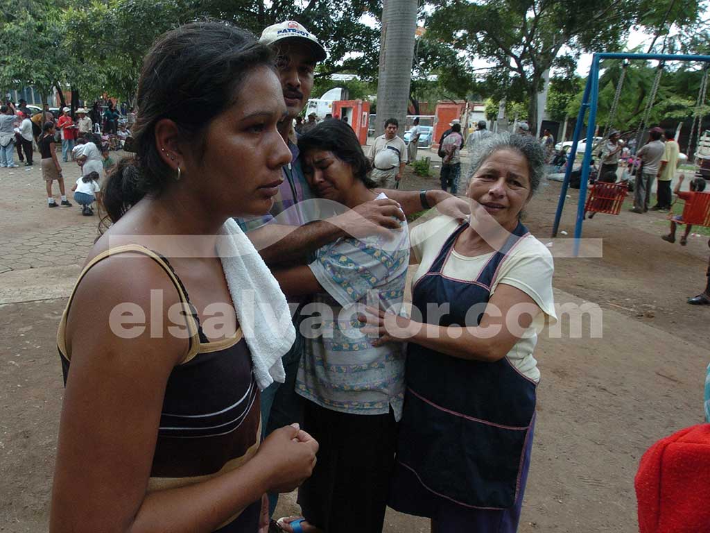 Tres mujeres abrazadas en un parque o zona al aire libre; la mujer del centro llora desconsoladamente mientras es sostenida por sus familiares.