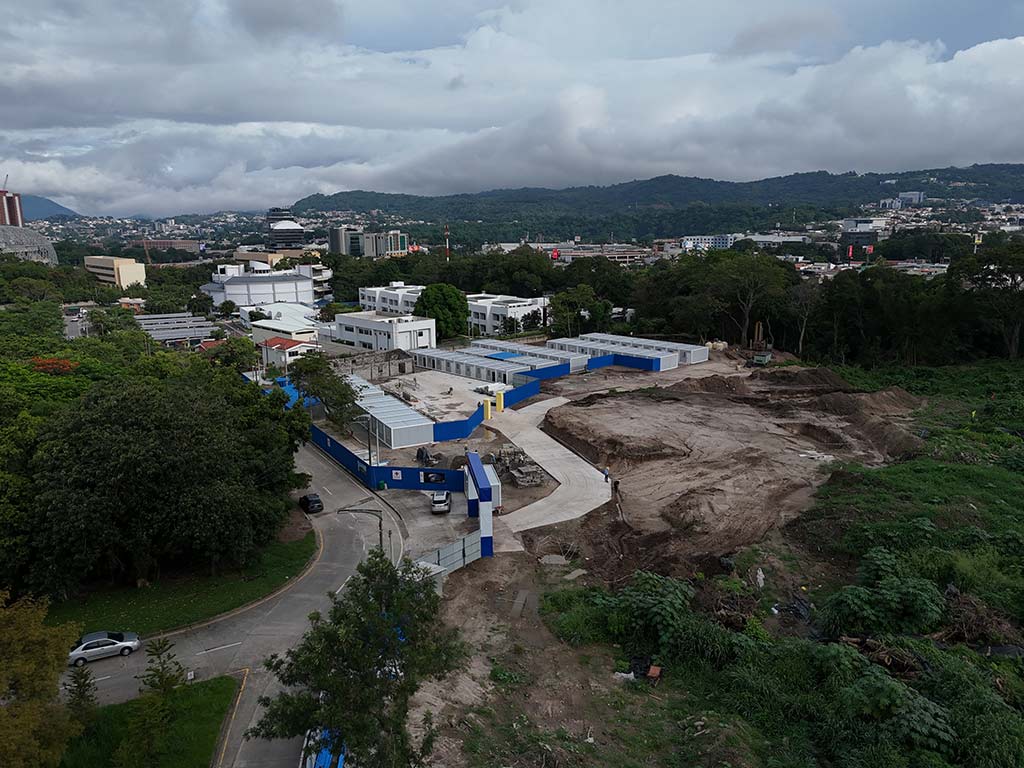Vista aérea con dron que muestra el predio en construcción del CIFCO, áreas verdes circundantes y el Estadio Nacional de El Salvador al fondo.