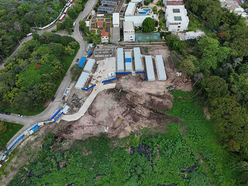 Vista aérea con dron que muestra el predio en construcción del CIFCO, áreas verdes circundantes y el Estadio Nacional de El Salvador al fondo.
