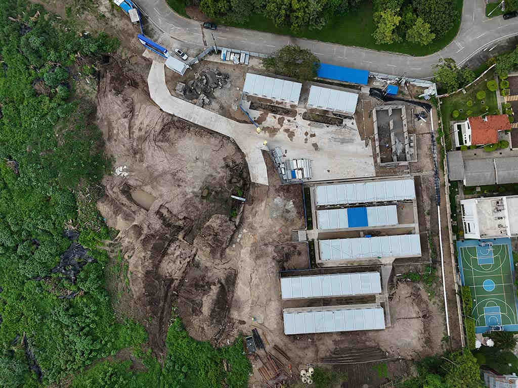 Toma cenital que muestra terracería intervenida, una rampa de concreto recién instalada, casetas operativas y trabajadores de la obra.