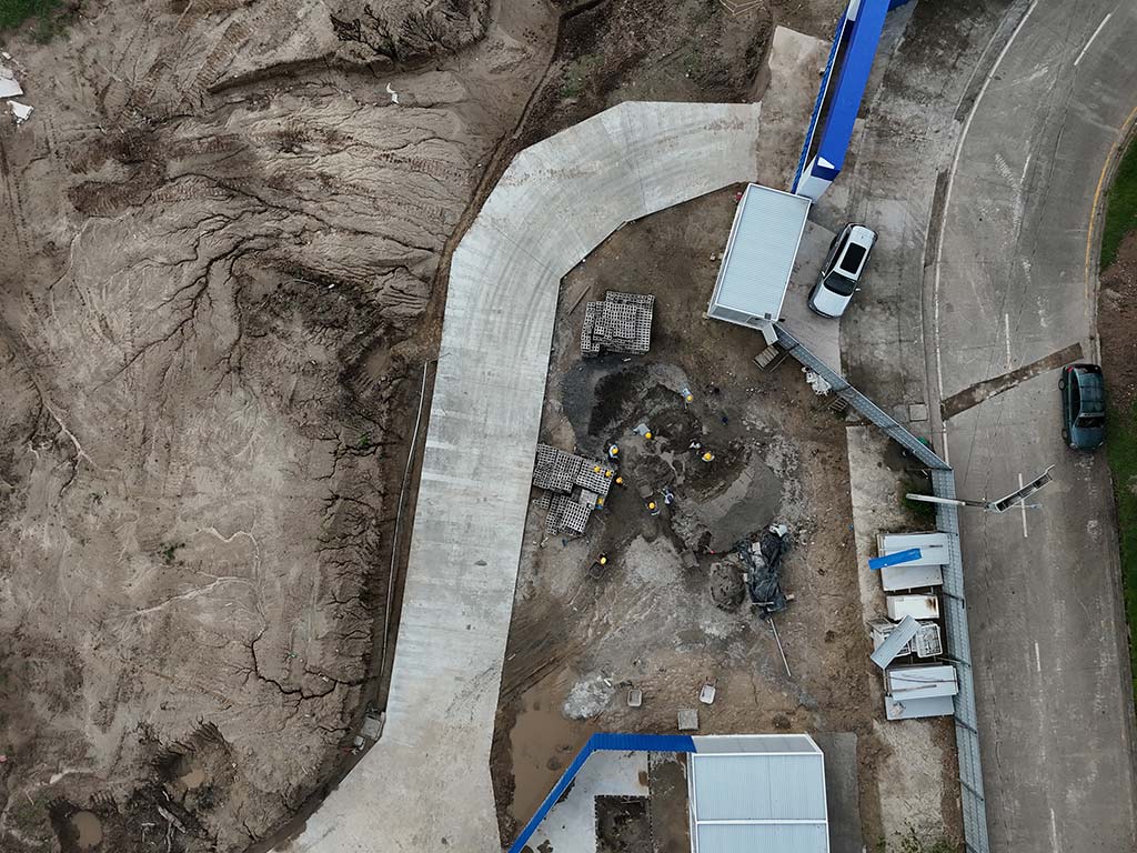 Toma aérea vertical que muestra excavaciones de terreno, una rampa de concreto y personal trabajando en el sitio de la obra. 