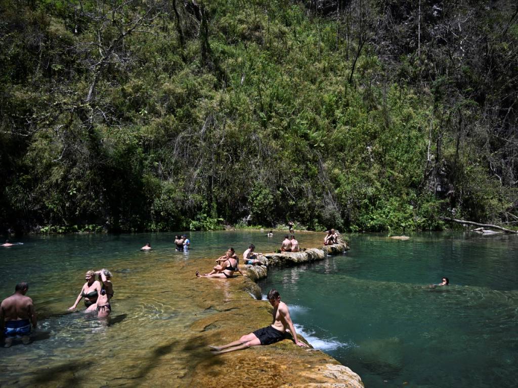 Grupo de personas nadando y relajándose en las pozas turquesa rodeadas de exuberante naturaleza.