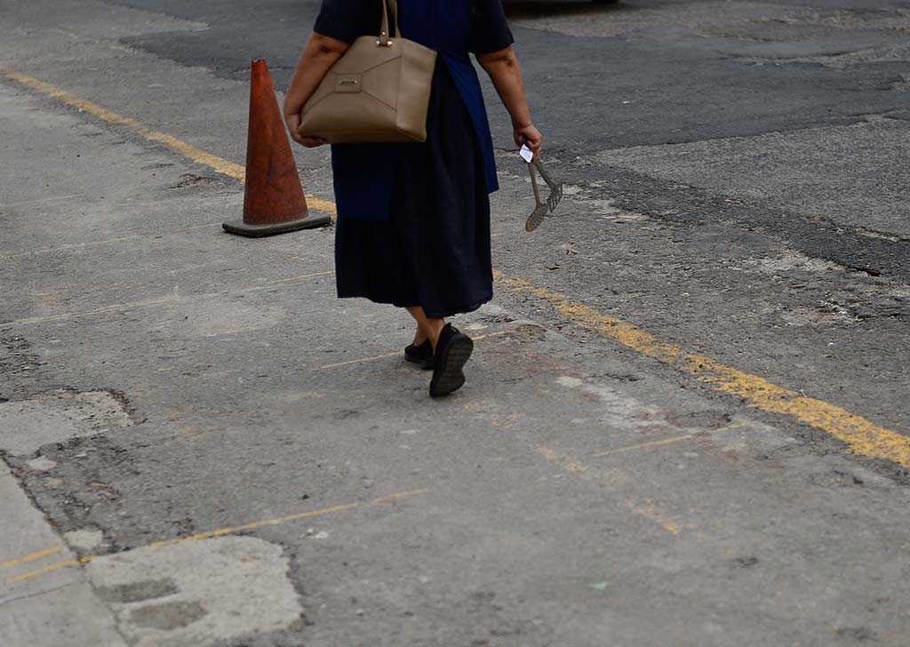 Plano detalle de las piernas de una persona caminando sobre una acera de concreto que muestra marcaciones de pintura amarilla descolorida.
