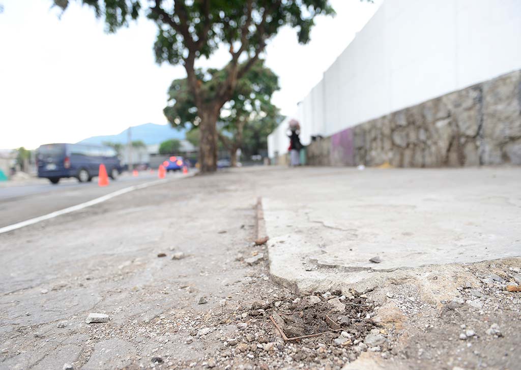 Toma a ángulo bajo del borde de una acera de concreto que muestra pequeños restos metálicos oxidados incrustados en el suelo.