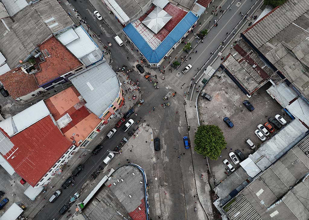Fotografía aérea en picado de una intersección urbana con calles despejadas, techos de edificios y algunos vehículos transitando.