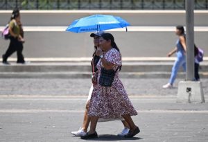 Una persona cubriéndose del sol directo con una sombrilla en las calles de la ciudad.
