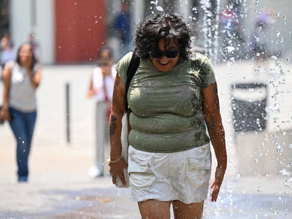 Una mujer caminando cerca de una fuente de agua para refrescarse durante un día caluroso en San Salvador.