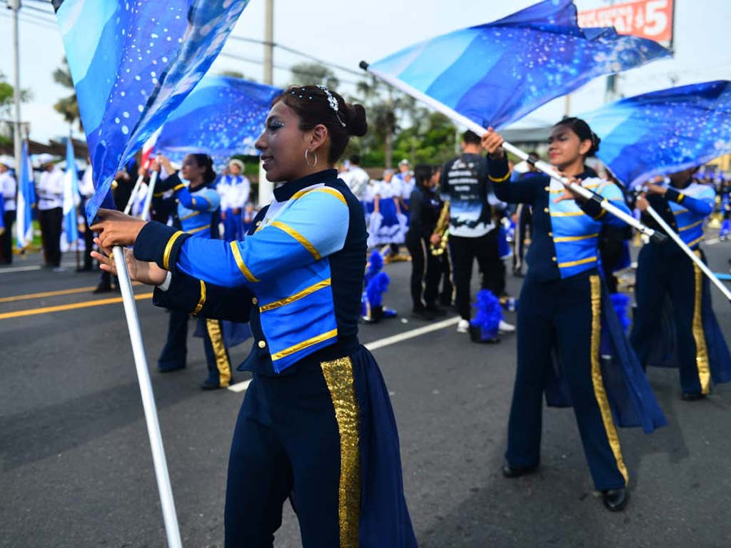 Una estudiante en primer plano sosteniendo el asta de una bandera azul decorada con destellos durante la presentación.