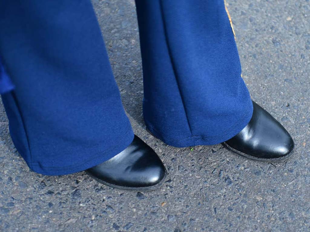 Acercamiento a los pies de una estudiante mostrando zapatos negros de vestir y el ruedo del pantalón azul.